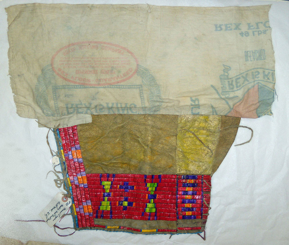 Indians who traded with European Americans received all kinds of manufactured goods in exchange for furs.  Indians sometimes re-used the goods in ways that better suited them.  These leggings were made by a Lakota woman, Anne Good Eagle.  She constructed the leggings with a cotton cloth flour sack from the Royal Milling Company and leather. She then decorated them with dyed porcupine quills. The leggings would have been tied around a woman’s legs.  Only the decorated leather would show below her skirt.  These leggings are in the collections of the SHSND Museum.
