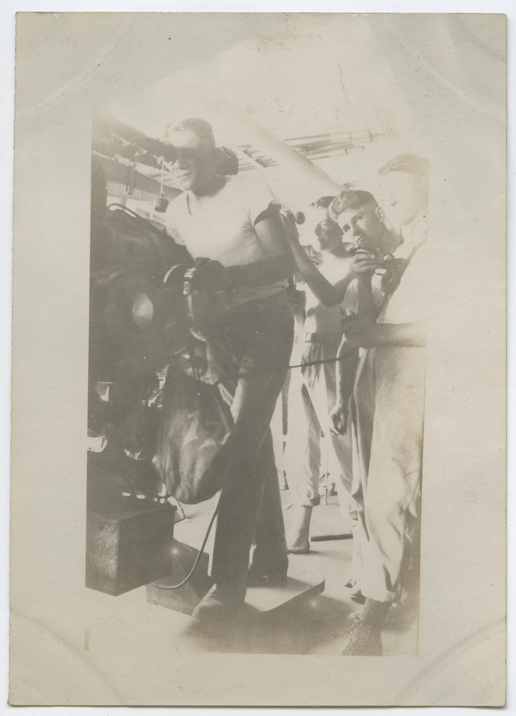 One man checks the sights on the guns while the man behind him reports to other members of the gunnery crew through a communications tube.