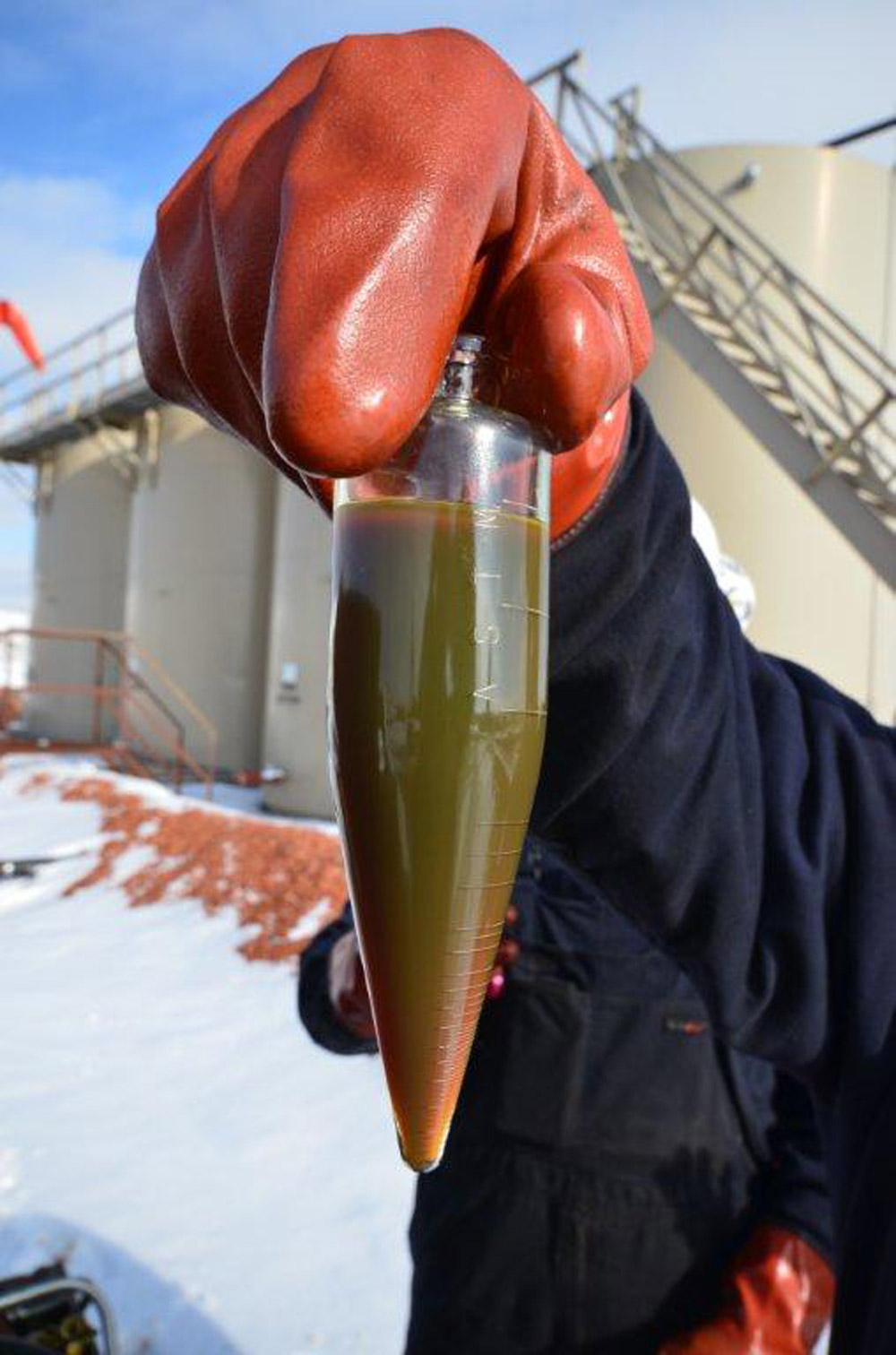 A worker holds a small container of Bakken oil.