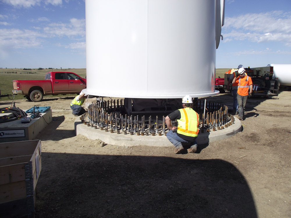 The first part of the wind tower is lowered onto the bolts and secured.