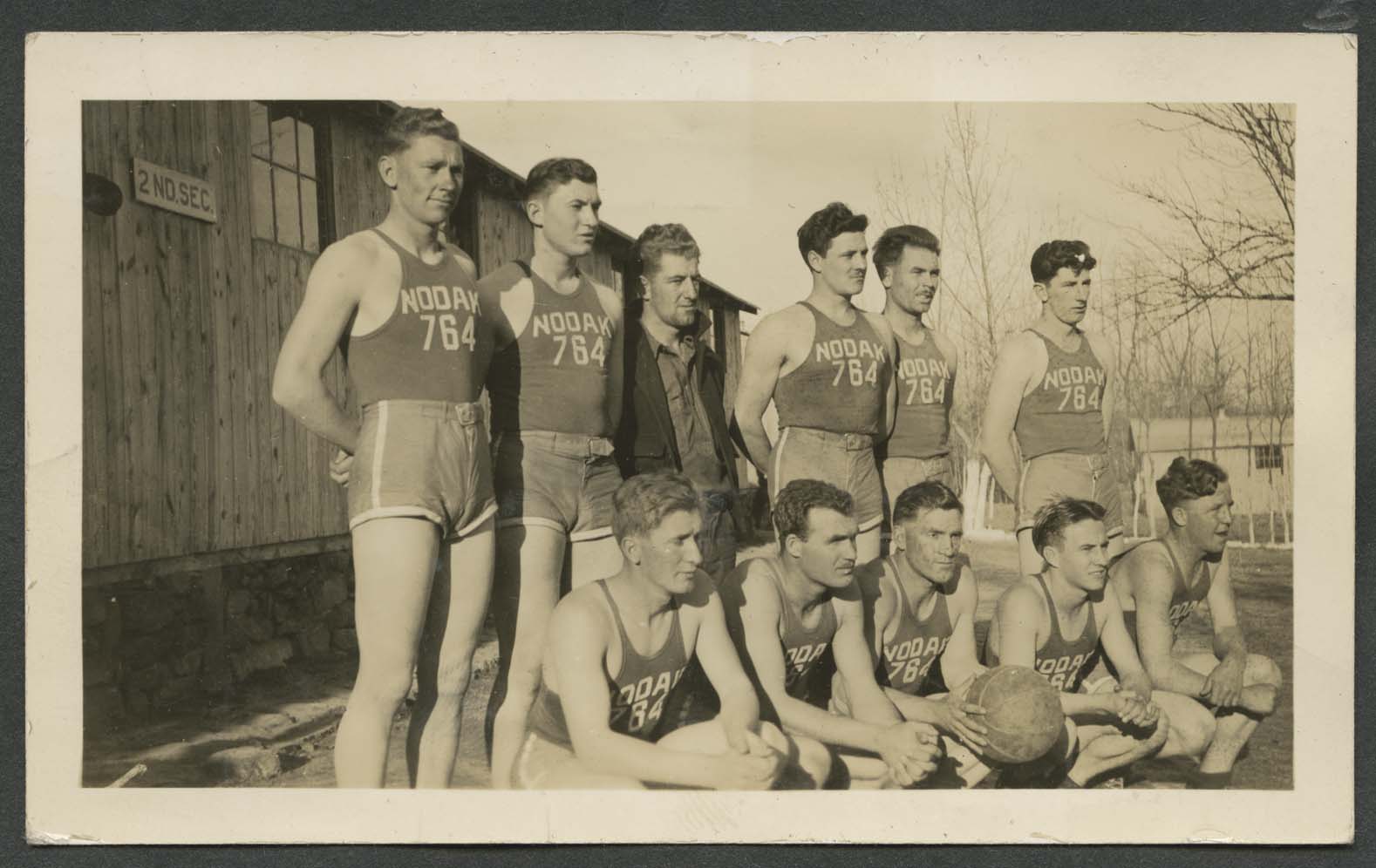 Basketball team stand near building with sign 2ND SEC, site unknown