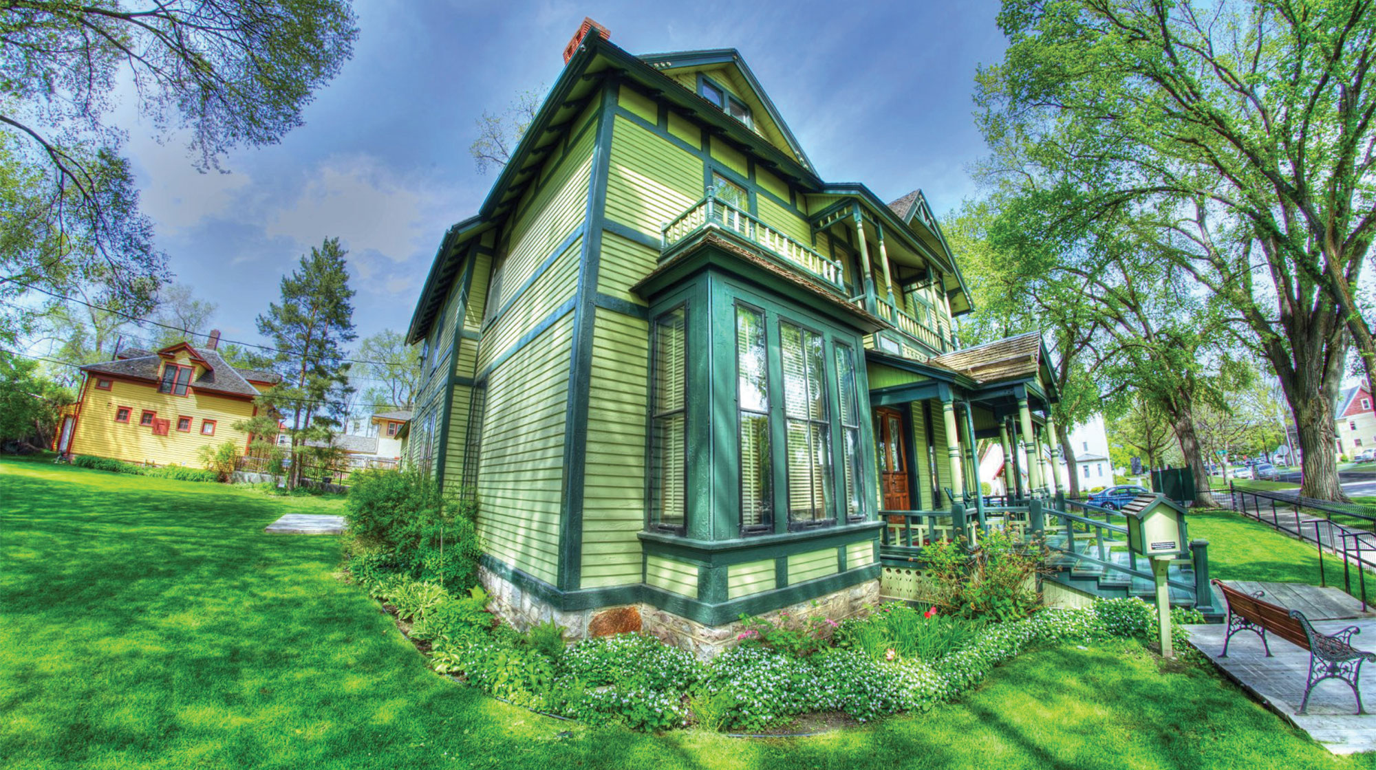 An old green house with a yellow cottage in the back