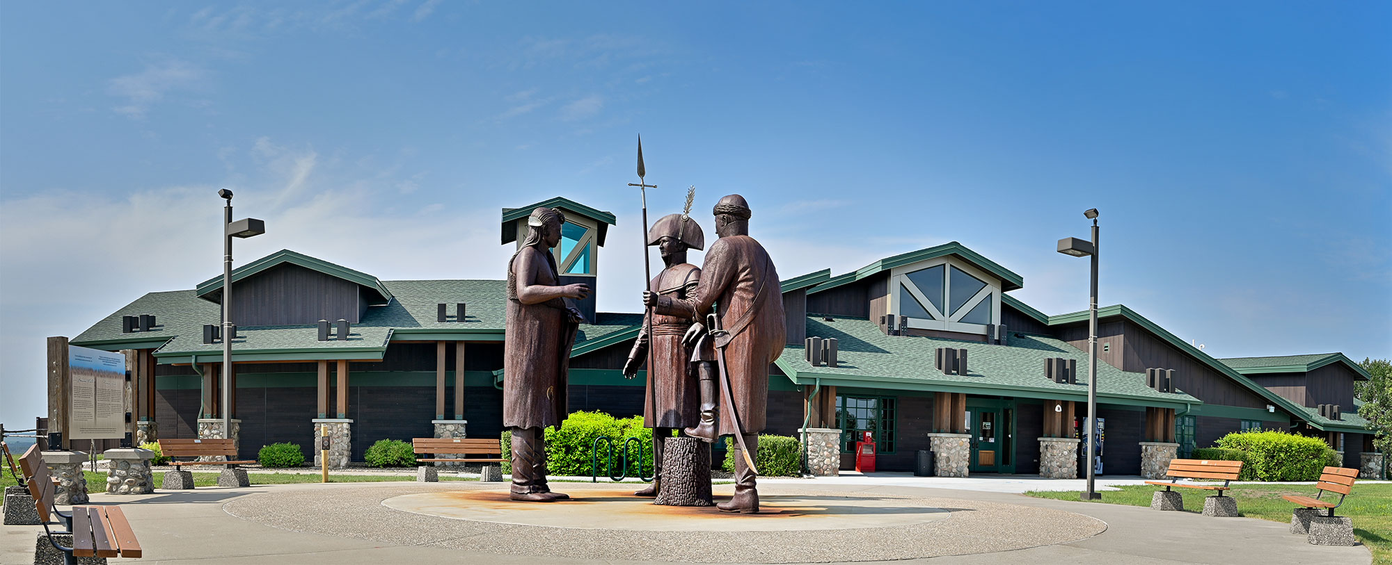 exterior view of a brown building with green trim and roof. Three statues stand in front of the building. They are of Lewis & Clark and a Native American 